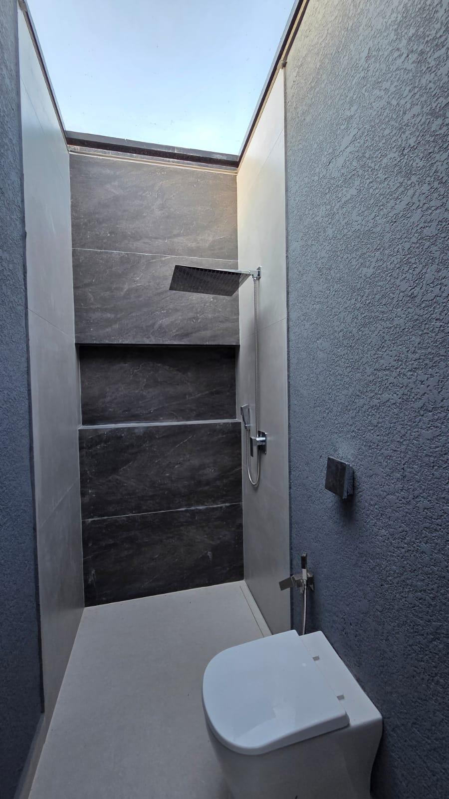 Banheiro com iluminação zenital, ducha higiênica e revestimento escuro