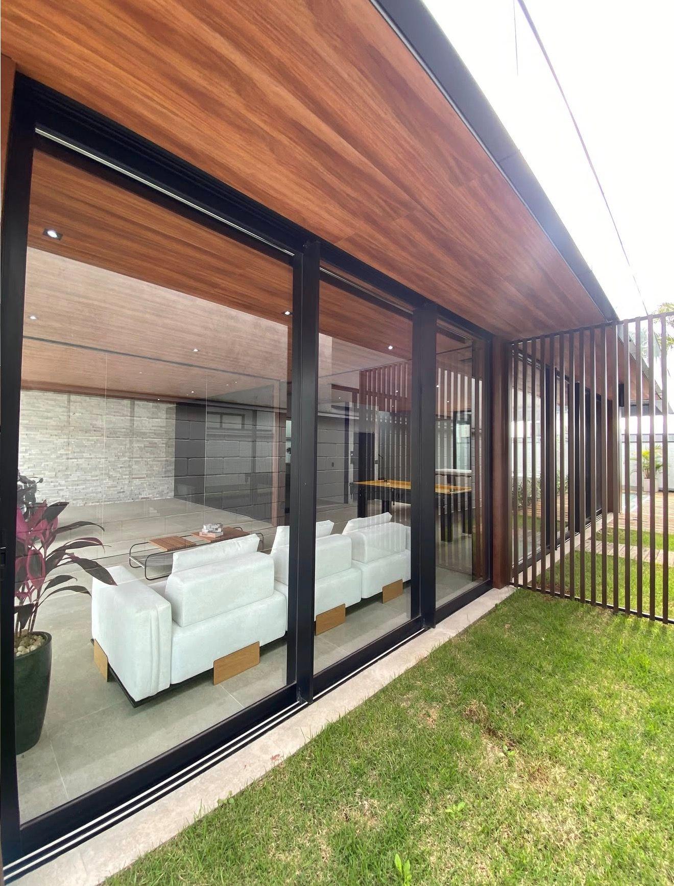Sala integrada vista do jardim, com forro amadeirado e grandes esquadrias